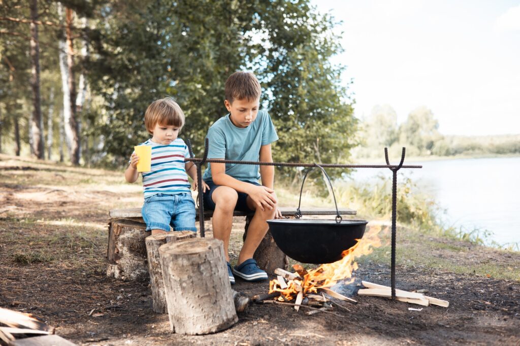 Children sitting around a campfire in forest in summer. Picnic outdoors. Camping life